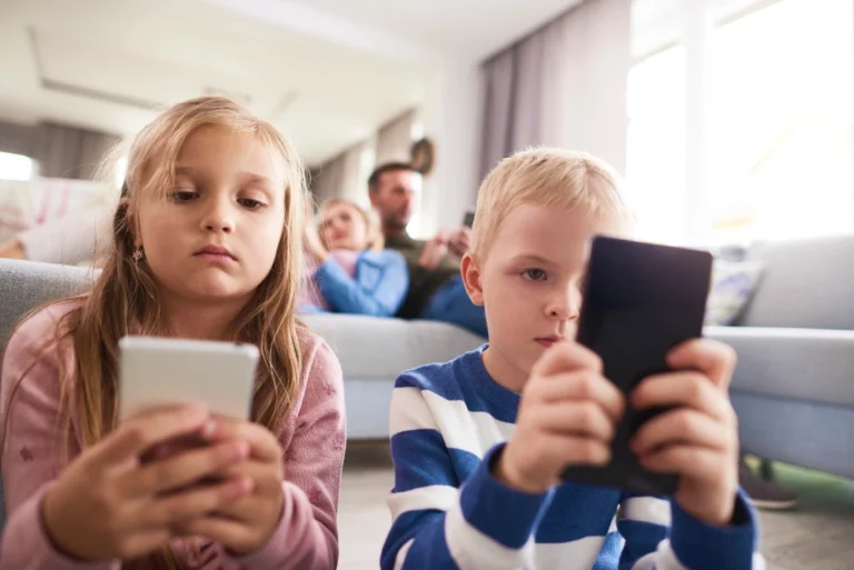 Children using tablets and smartphones in living room while parents sit on couch in background also on their phones