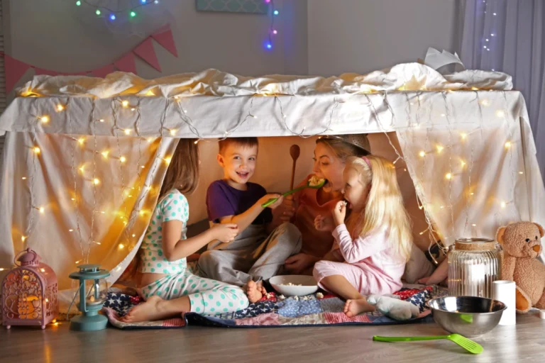 Mother and children playing together in blanket fort decorated with fairy lights during winter break"
